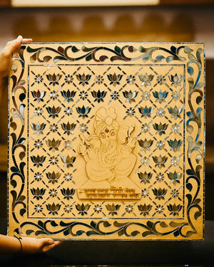 Decorative panel with intricate carvings of a deity and floral patterns, held by a hand.